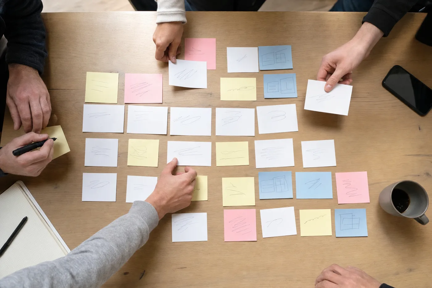 Overhead view of a team arranging printed cards and sticky notes on a large desk while planning training formats