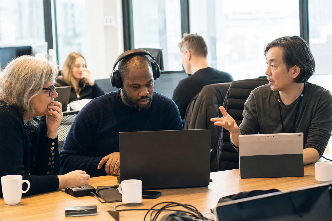 Coworkers collaborate during an accessible employee training session in a bright office, one wearing headphones at a laptop
