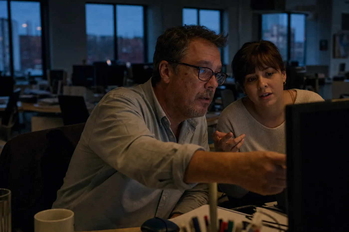 Two coworkers reviewing an AI tool together at a monitor in a quiet evening office