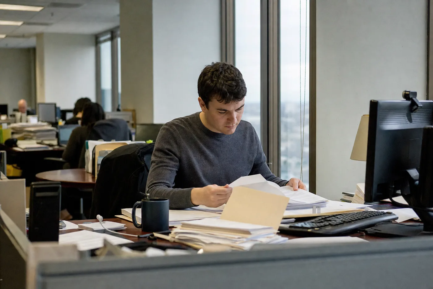 New employee sitting alone at a desk in their first week, working through a stack of printed paperwork