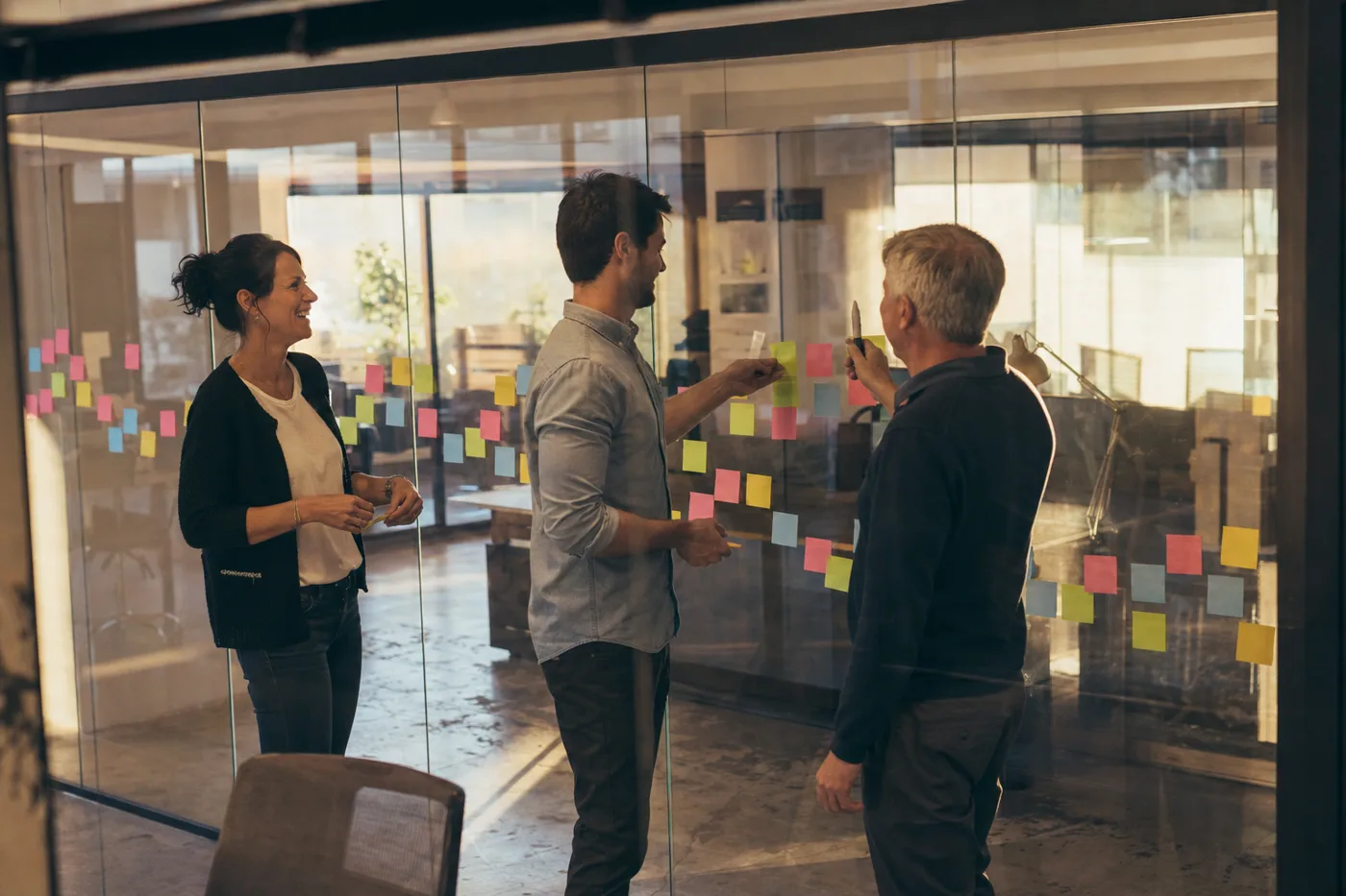 HR team arranging sticky notes into a 90-day onboarding journey on a glass office wall