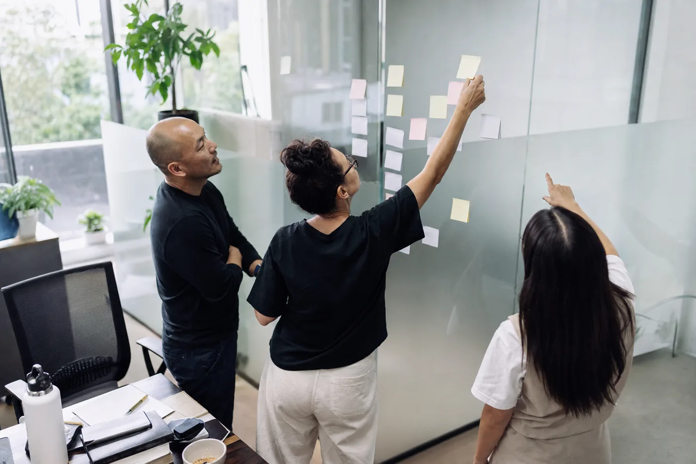 Coworkers mapping out practice scenarios on blank sticky notes at a glass wall to plan a skills rehearsal program