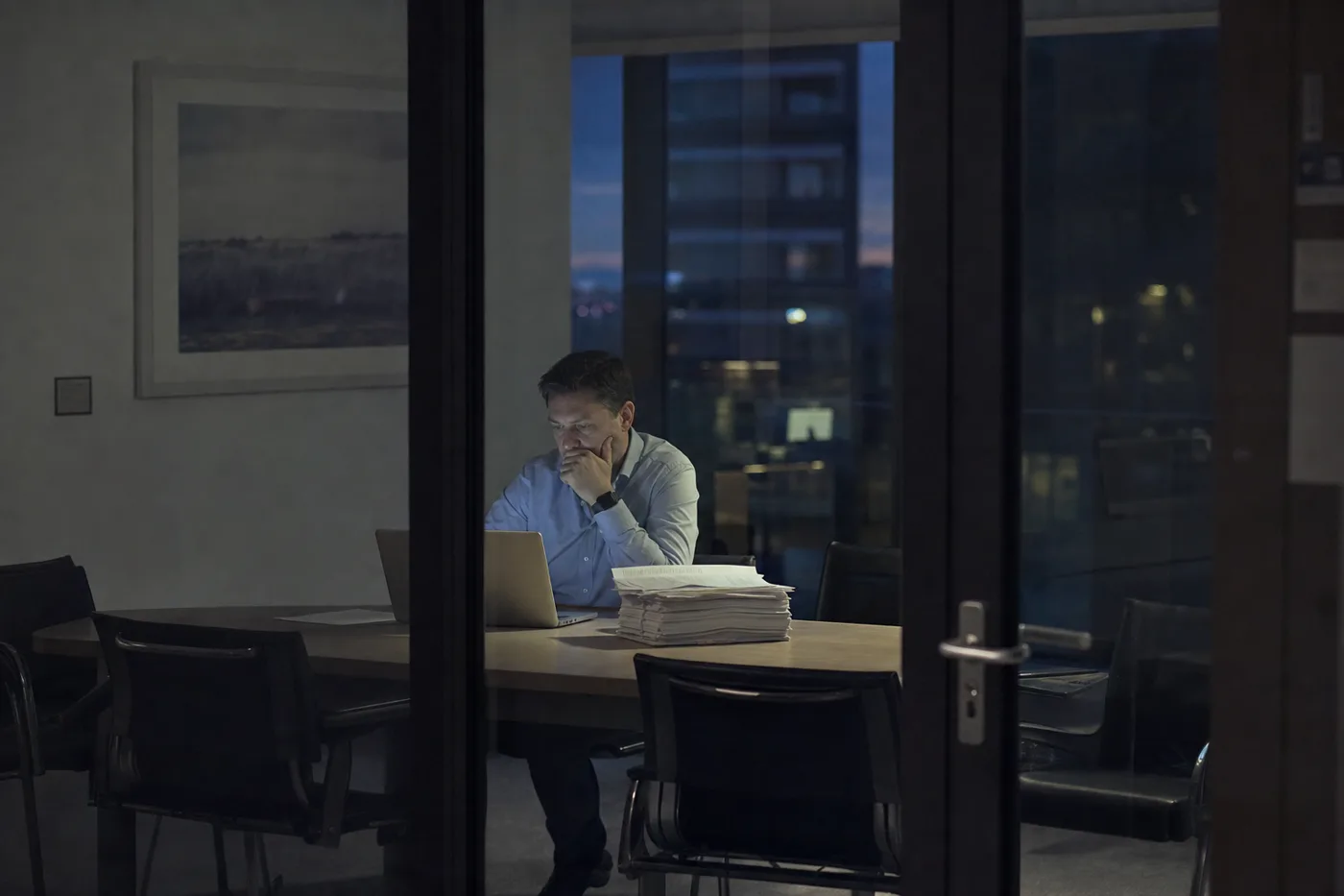 Hiring manager alone in an interview room after hours, weighing the cost of recruiting scarce AI talent
