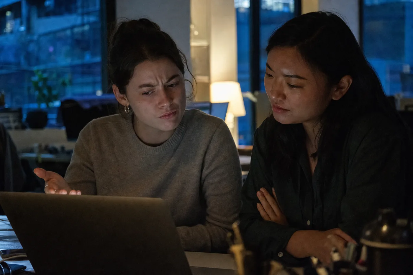 Two coworkers stress-testing an AI tutor's feedback together at a laptop in the evening