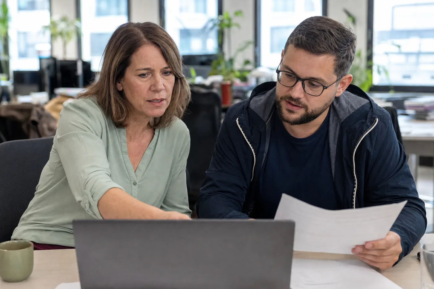 An L&D manager and an IT security colleague reviewing an AI training data privacy policy together on a laptop in a bright office