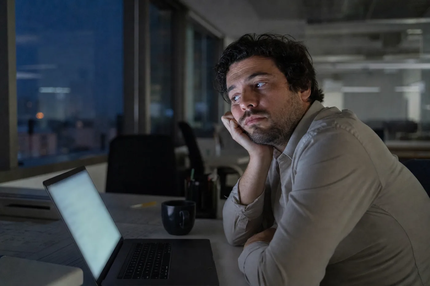 An employee half-ignoring a training chatbot on a laptop in a dim office, illustrating passive AI tutoring