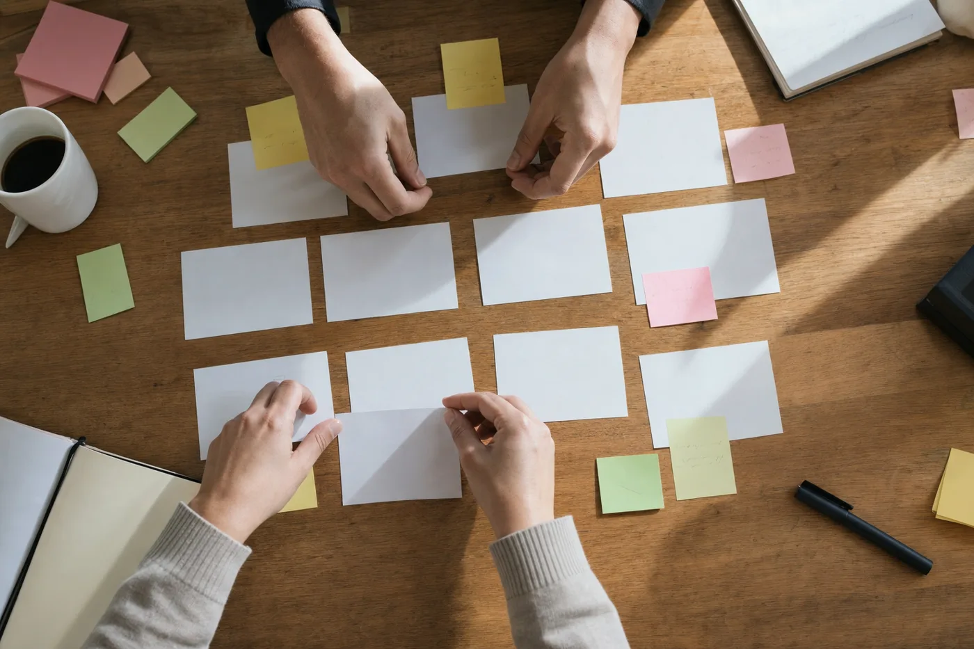 Overhead view of hands arranging index cards and sticky notes on a wooden desk to map out a training plan