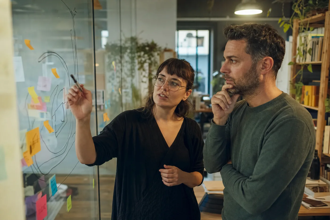 Two coworkers mapping a corporate training disruption strategy on a glass wall in a bright office