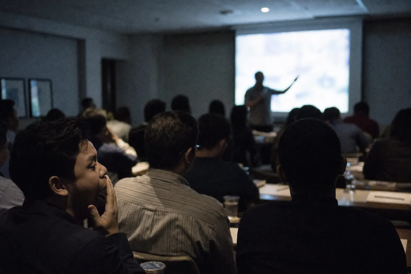 Employees watching a polished presentation in a dim conference room, absorbed but passive