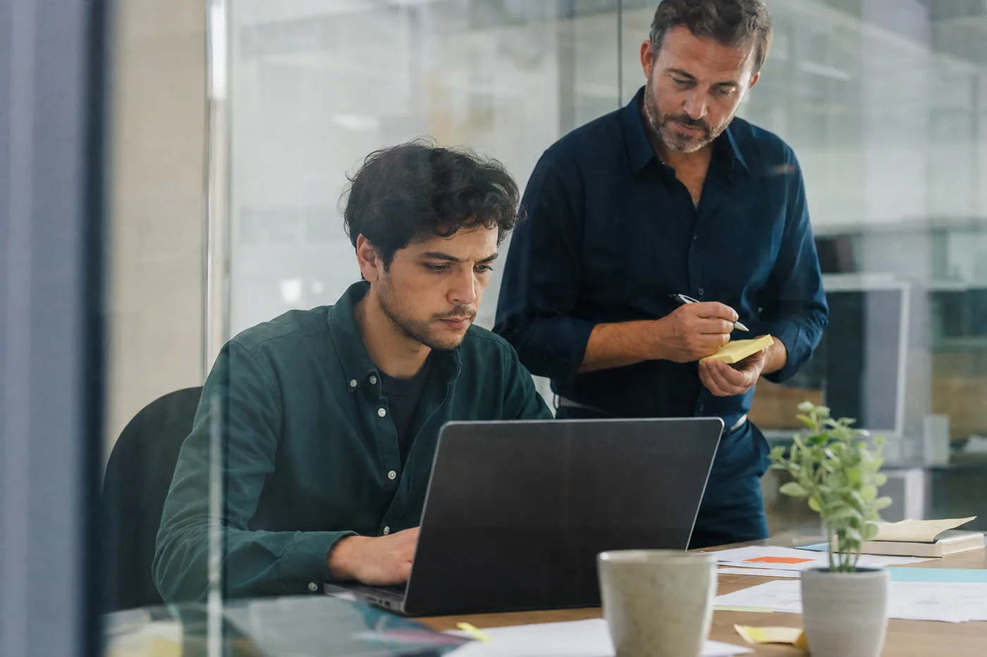 New hire working through a task at a desk while a colleague observes and takes notes
