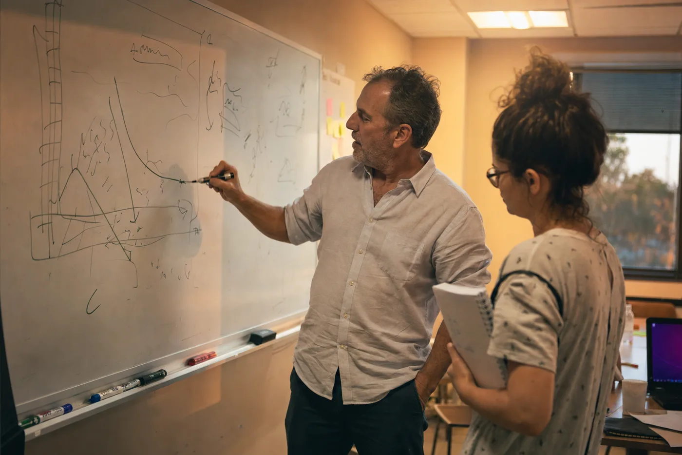 Two coworkers sketch a steep forgetting curve on a whiteboard during a training planning session