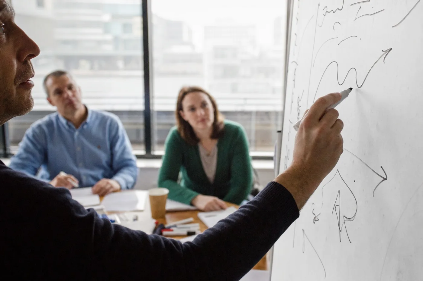 Trainer sketching a rising learning curve on a whiteboard while colleagues watch during a workshop