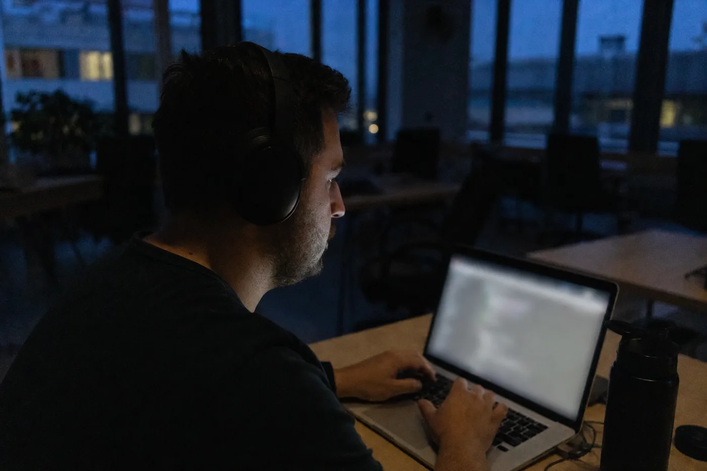 Employee practicing a work scenario on a laptop in a dim evening office, lit by the screen