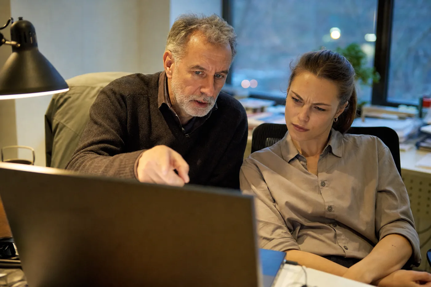 Two coworkers practicing an AI verification exercise together at a laptop in warm evening light