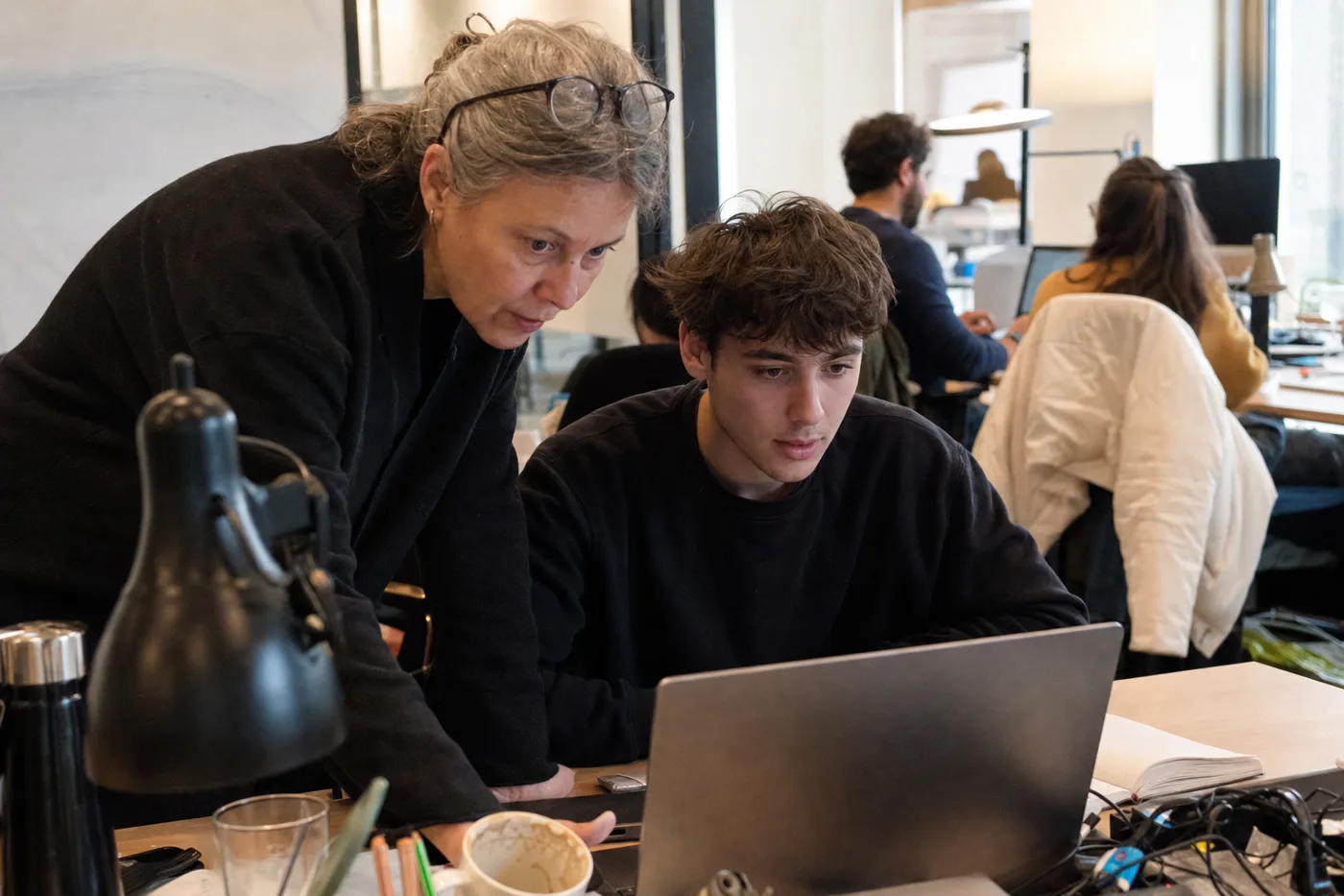 Senior engineer coaching a new hire through entry-level training at a shared desk