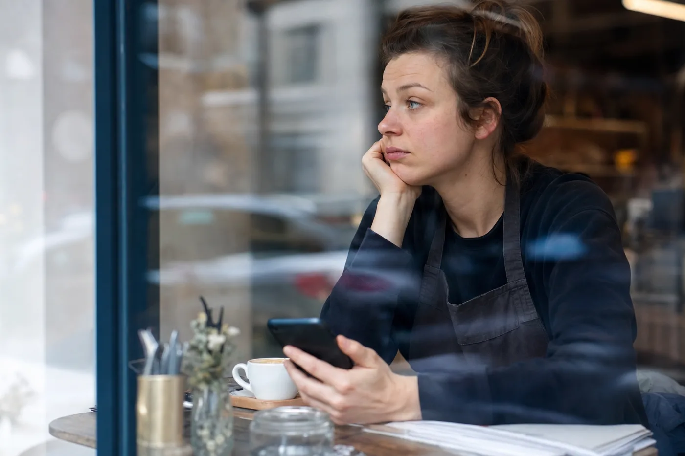 A retail employee on a short break at a cafe table with her phone, the few spare minutes that frontline worker training has to fit into
