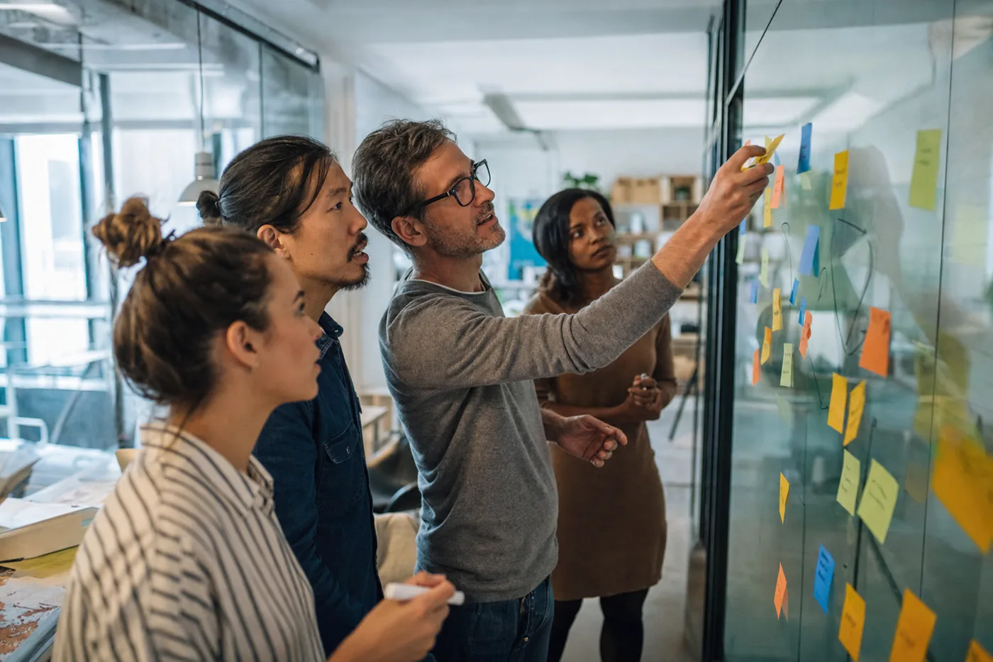 L&D team planning a gamification in training program on a glass wall covered in sticky notes in a bright office