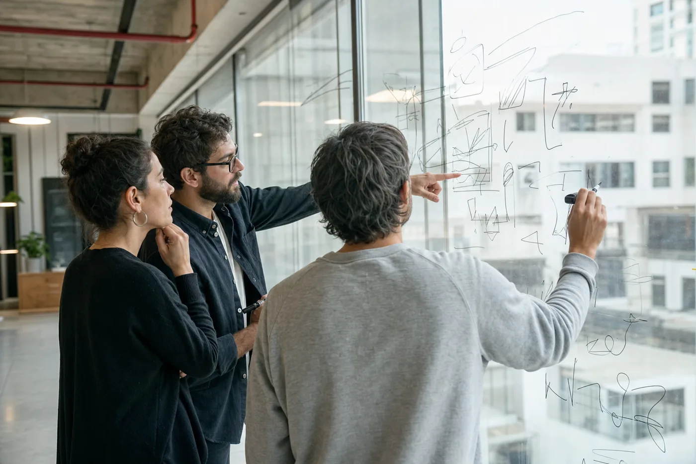 Coworkers gathered around a glass wall covered in hand-drawn diagrams during a workshop