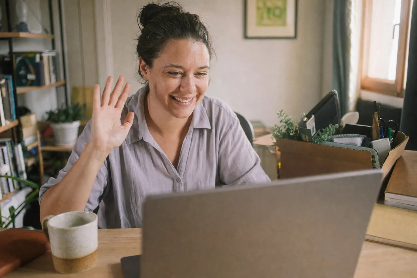 New hire waving to teammates on a video call during remote employee onboarding from a home office