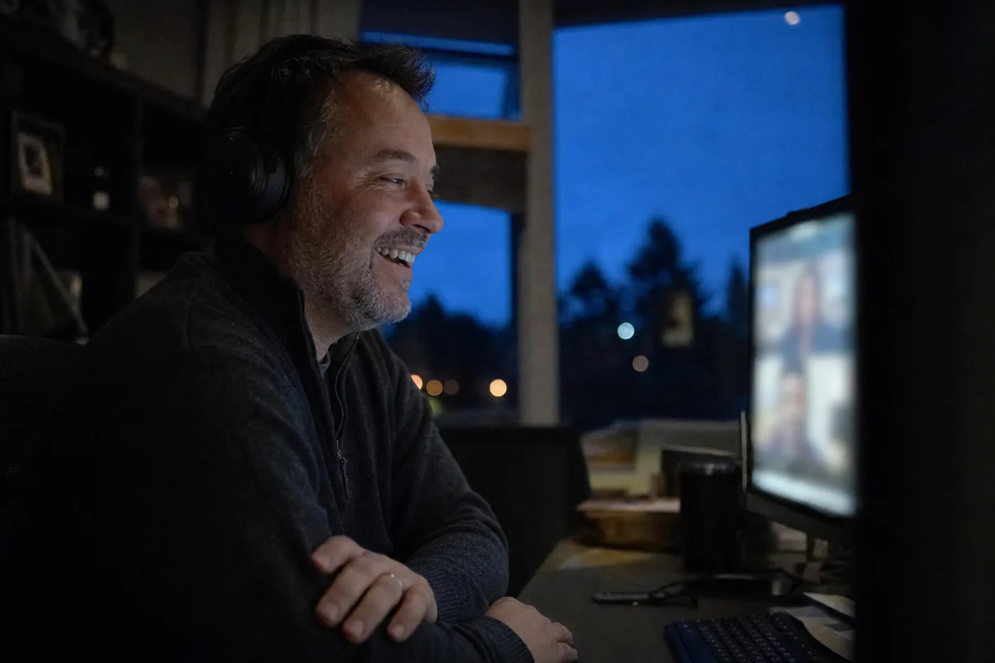 An onboarding buddy laughing with a remote new hire during an evening video call