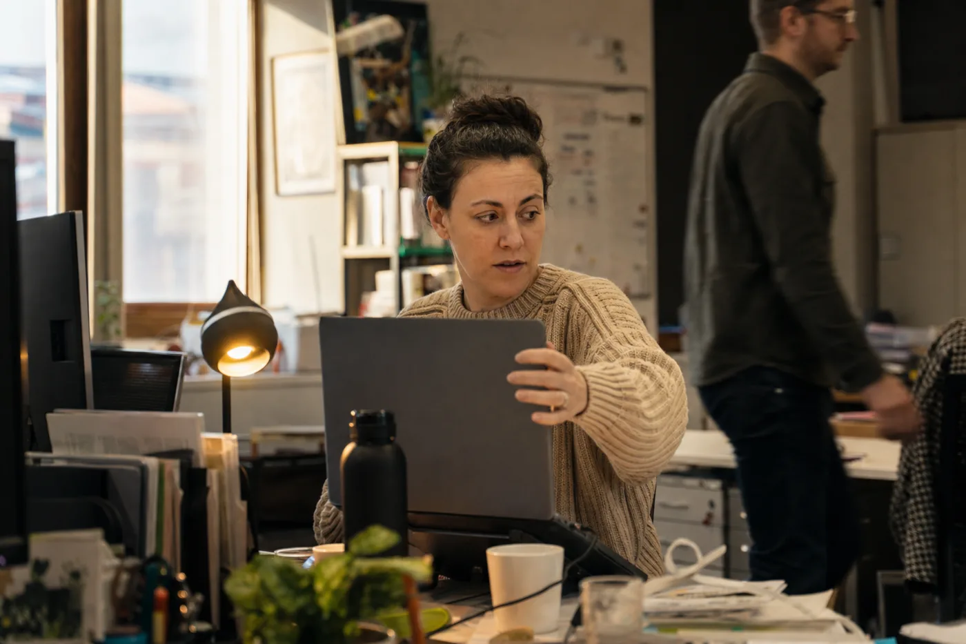 An employee quietly using shadow AI at work, angling a laptop screen away from a passing coworker