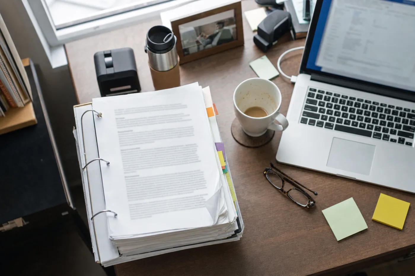 Overhead view of a desk where a printed AI policy binder sits unread beside a laptop