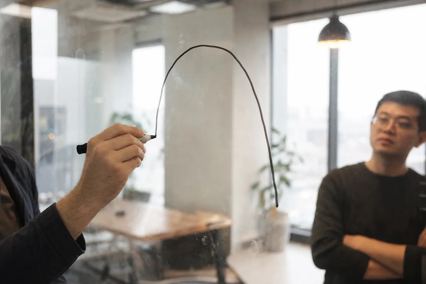 A person sketching a loose upside-down curve by hand on a glass office wall, mapping the sweet spot where challenge stays productive