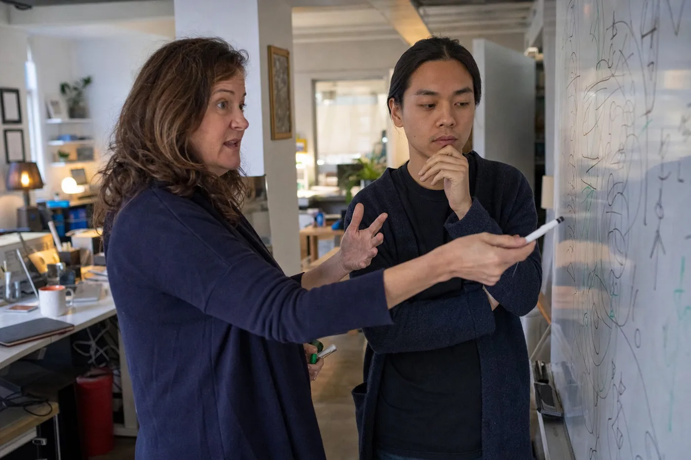 Trainer using Socratic questioning in training, posing a question at a whiteboard while a colleague reasons through the answer