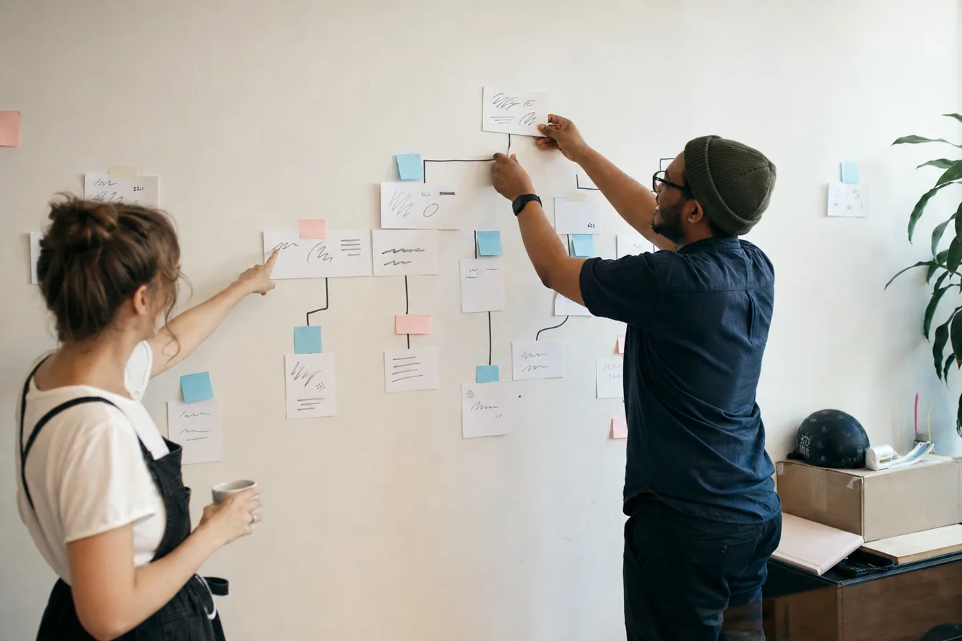 Two coworkers arranging printed cards and sticky notes on an office wall while designing a question-first training flow