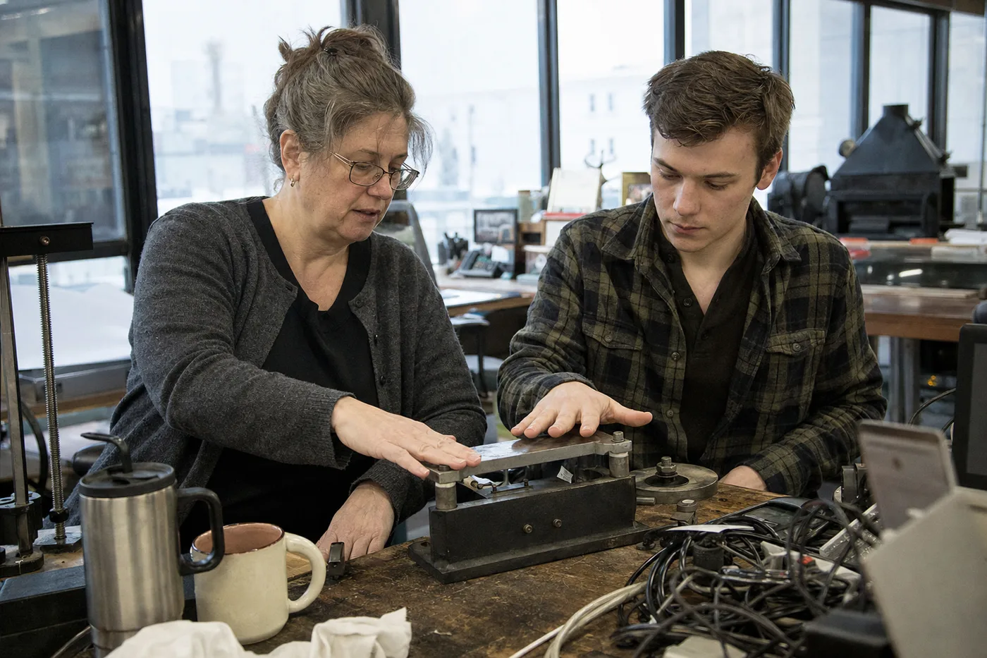 A veteran employee gives a colleague a hands-on refresher at a workbench, the kind of practice that prevents workplace skill decay