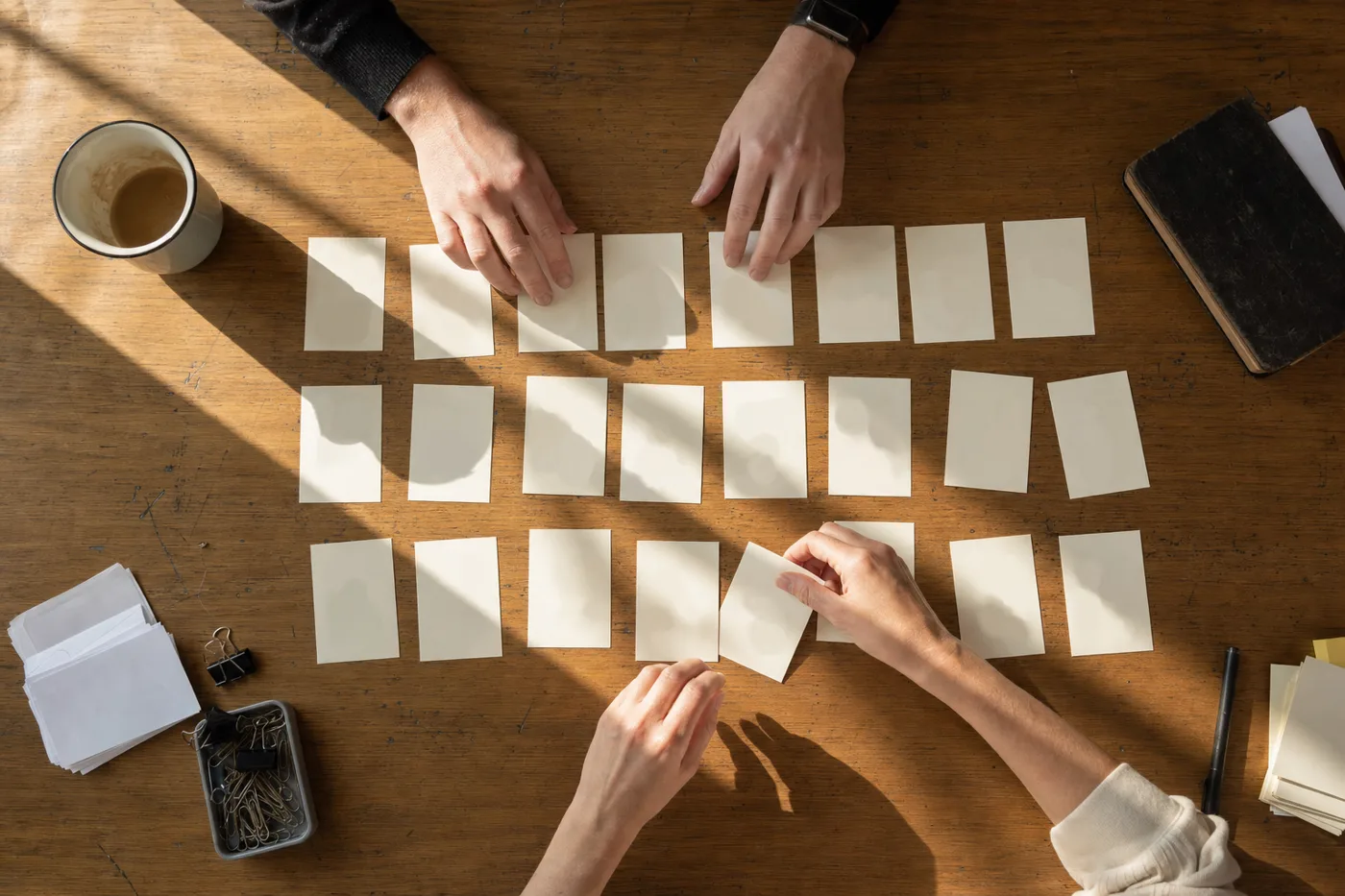 Hands arranging practice cards into spaced rows on a desk in early morning light, a simple spaced practice system against skill fade